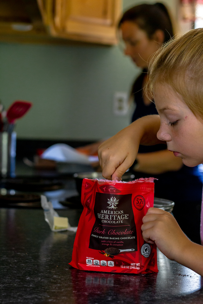 Image shows a young girl scooping dark chocolate form a pouch at a counter
