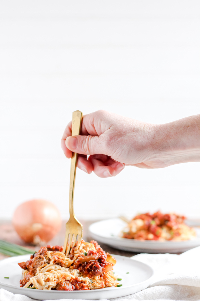 Photo shows a hand taking a bite of baked spaghetti