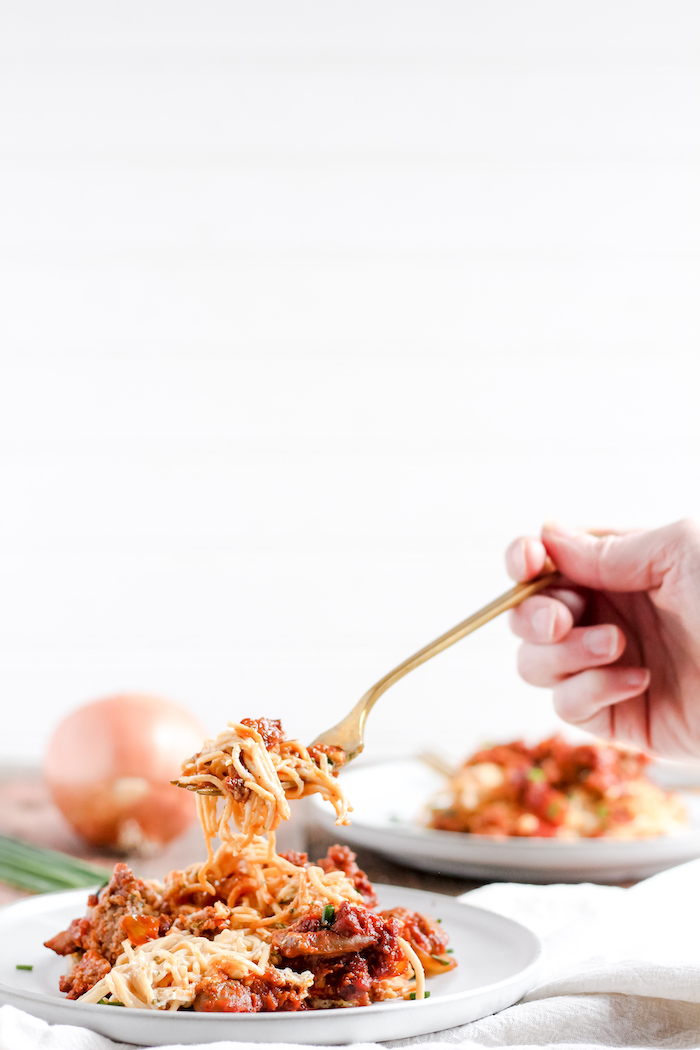 Image shows a hand taking a bite of spaghetti casserole