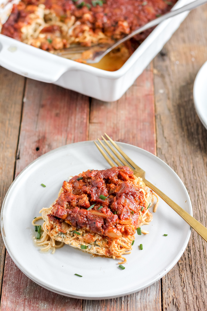 Image shows a plate of spaghetti casserole on a table next to a pan of casserole