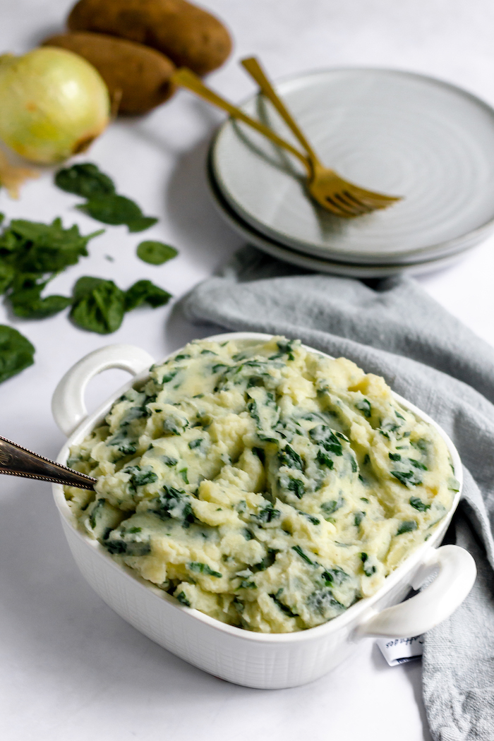 Images shows a dish of spinach mashed potatoes on a table next to an empty plate