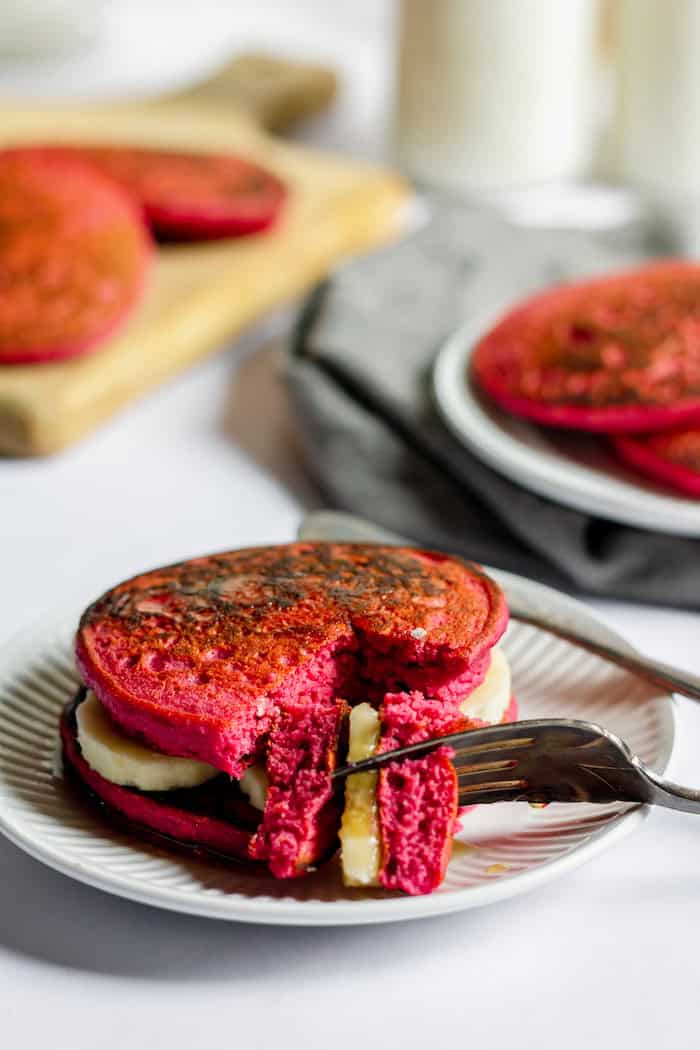 Image shows a plate of beet pancakes with bananas in between then on a plate