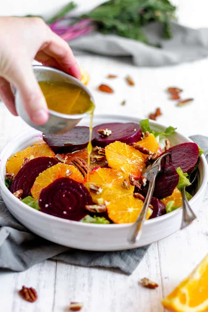 Image shows a bowl of roasted beet and citrus salad with a hand pouring dressing onto it