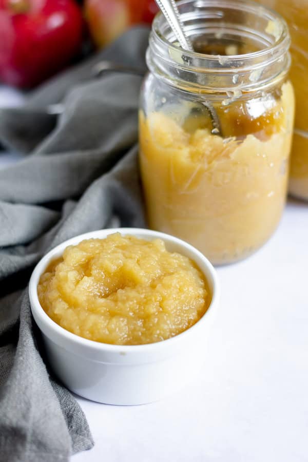 Image shows a jar of apple sauce with a spoon next to a bowl of apple sauce