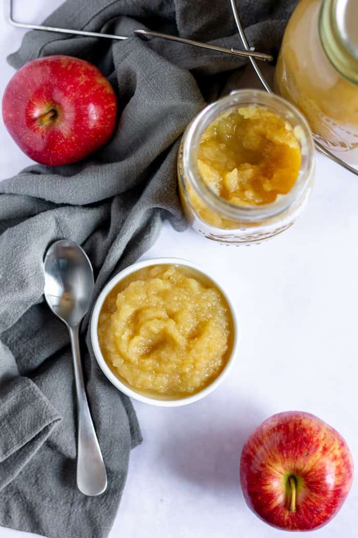Photo shows a bowl of apple sauce and jar of apple sauce taken from above.