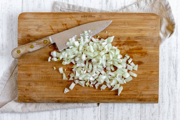 Image, taken from above, shows diced onions and a knife on a cutting board. 