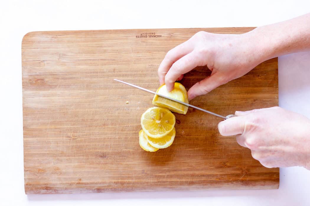 Image, taken from above, shows a hand slicing lemons