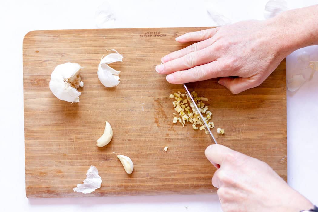 Image, taken from above, shows a hand dicing garlic into small pieces