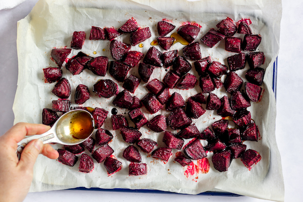 Image, taken from above, shows a cookie sheet full of diced beets being drizzled in oil.