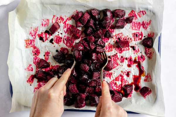Image, taken from above, shows hands tossing the beets after being drizzled in balsamic and oil