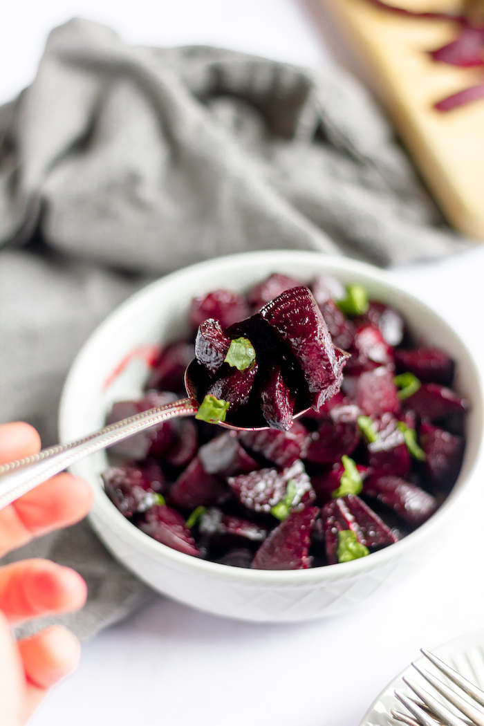 Image shows a spoon full of beets over a small bowl of balsamic roasted beets on a table