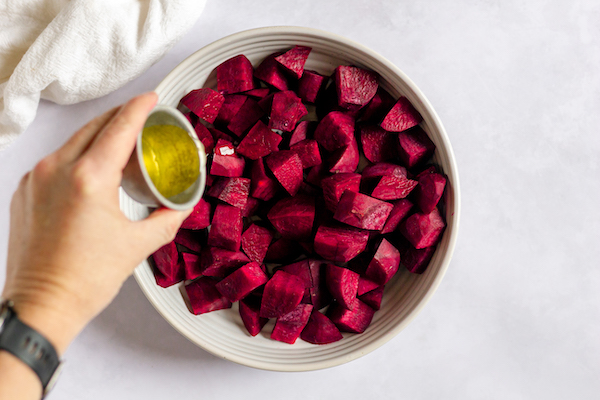 Image, shows a bowl of beets with olive oil being poured over them.