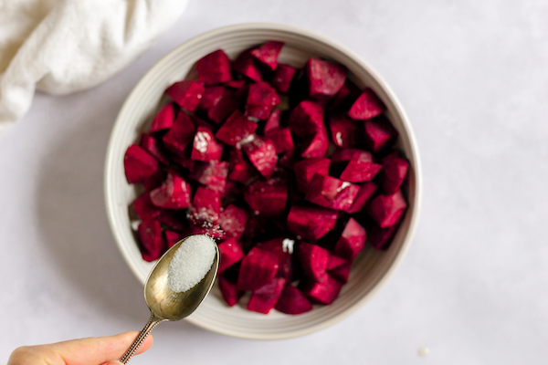 Image, taken from above, shows a bowl of diced beets with a spoon sprinkling salt over them.
