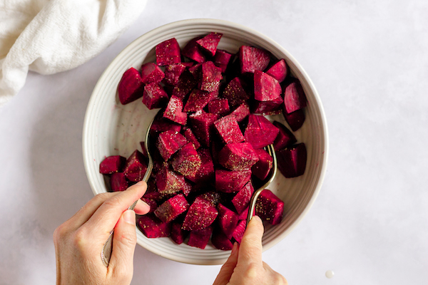 Image, taken from above, shows two spoons tossing the beets together.