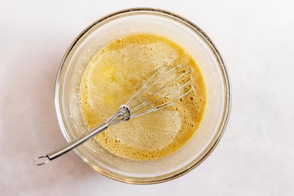 Image, taken from above, shows a glass mixing bowl with a whisk sitting in the bowl and batter. 