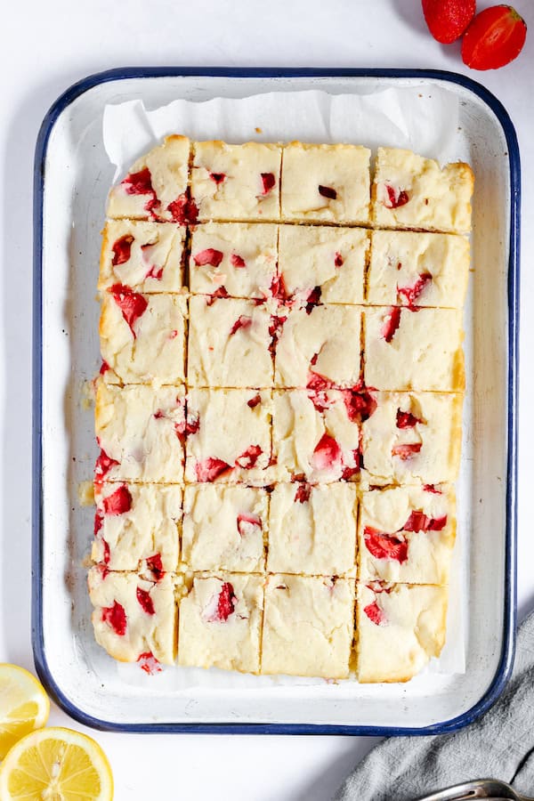 Image, taken from above, shows the strawberry lemon blondies after baking, cut into pieces in a white pan