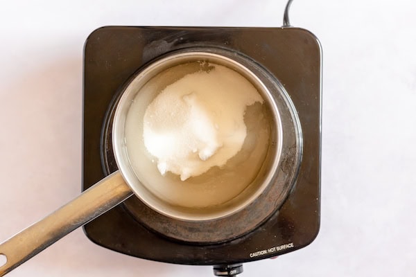 Image, taken from above, shows a small saucepan on heat with water and sugar in it.