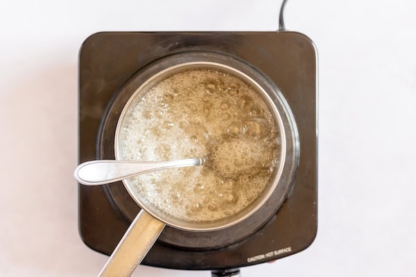 Image, taken from above, shows a small saucepan on heat with water and sugar boiling in it.
