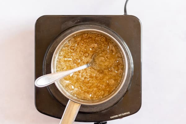 Image, taken from above, shows a small saucepan on heat with water and sugar boiling harder in it.