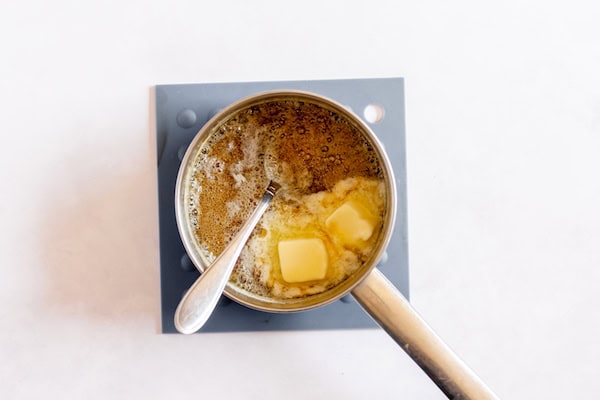 Image, taken from above, shows a small saucepan removed from heat with butter and sugar added to it.