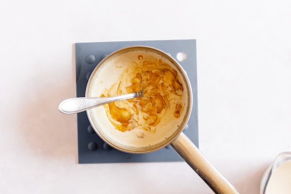 Image, taken from above, shows a small saucepan removed from heat with butter and sugar being mixed into it.