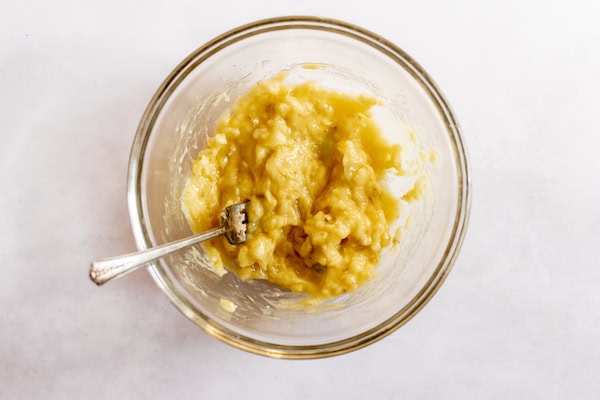 Image, taken from above, shows a glass bowl with mashed bananas in it.