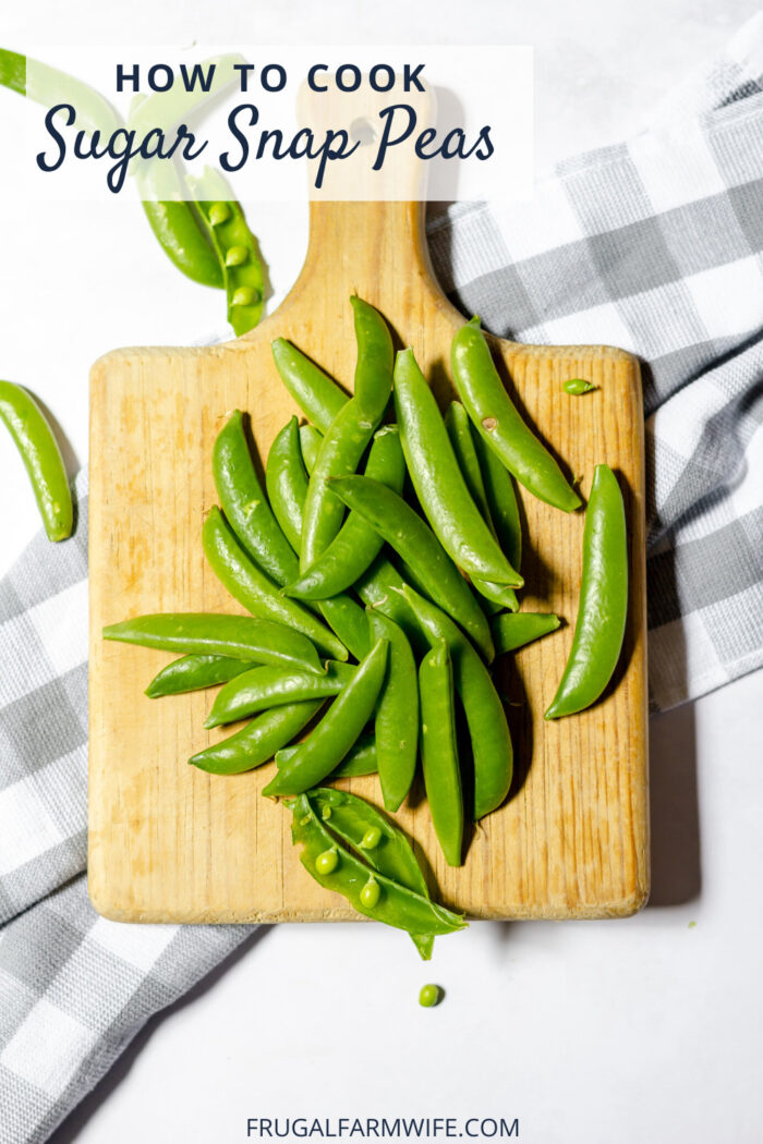 Photo, taken from above, shows a pile of sugar snap peas on a wood cutting board.
