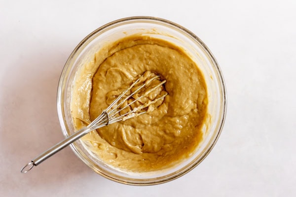 Image, taken from above, shows a glass mixing bowl with a whisk resting in it after the flours have been added in to the batter. 