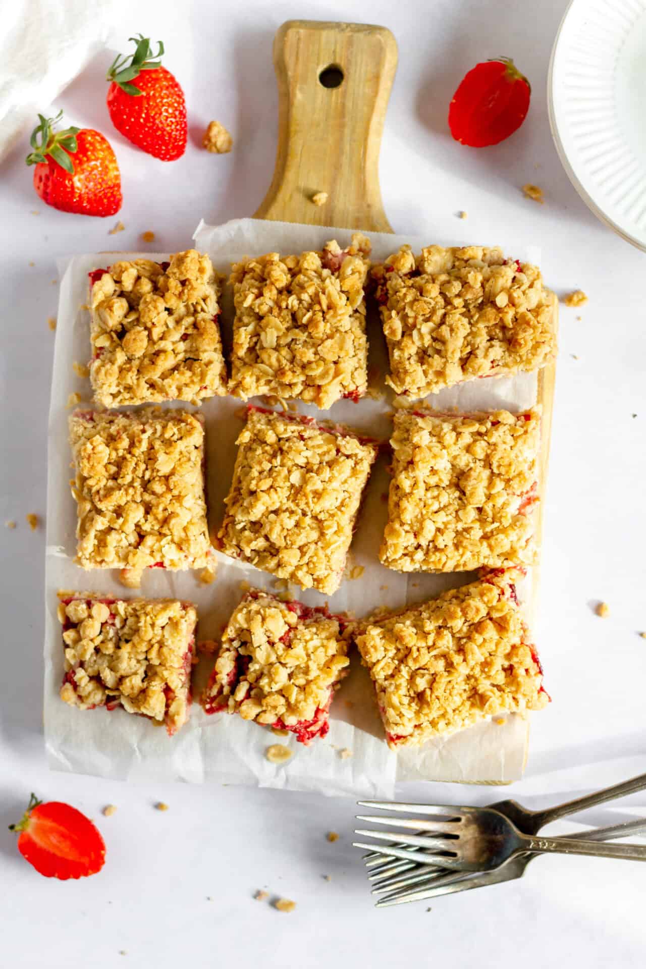 Image shows nine gluten free strawberry oatmeal bars on parchment paper on a small wood cutting board. 