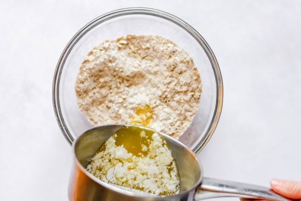 Image, taken from above, shows a small saucepan pouring melted butter into a glass bowl of mixed dry ingredients.