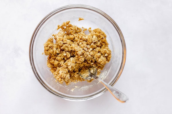 Image, taken from above, shows a spoon mixing the butter with the dry ingredients to make gluten free strawberry granola bars. 