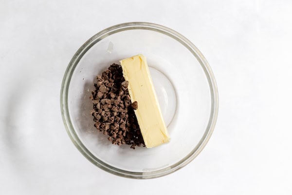 Image, taken from above, shows a glass bowl with a stick of butter and chocolate chips in it.