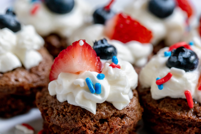 Image shows a close up of several gluten free brownie bites with frosting, blueberry and strawberry