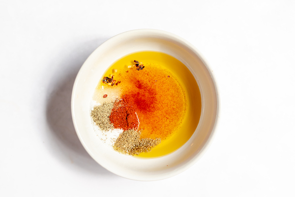 Image shows a white bowl photographed from above full of oil and the seasonings needed to make coleslaw without mayo