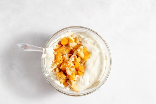 Image, taken from above, shows crumbled peach cobbler folded into the ice cream bowl.