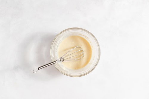 Image shows a glass measuring cup full of the cobbler ice cream ingredients and a whisk.