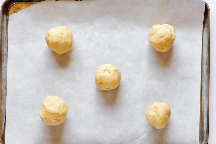 Image, taken from above, shows a cookie sheet with 5 cookie dough balls spaced on the pan. 
