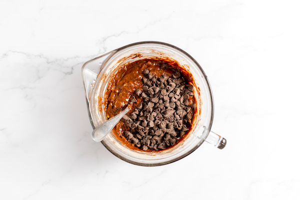 Images shows a glass mixing bowl with chocolate chips added to the batter