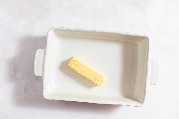 Image shows a white casserole dish sitting on a counter, with a stick of butter to be melted in the center. 
