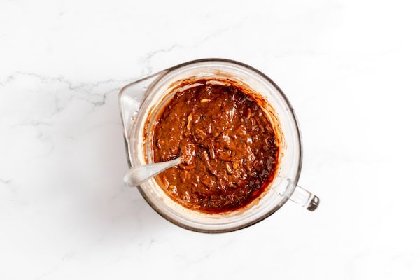 Image shows a glass mixing bowl with the zucchini batter mixed together
