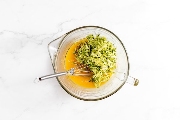 Image shows a glass mixing cup with the the zucchini ready to be whisked into the batter