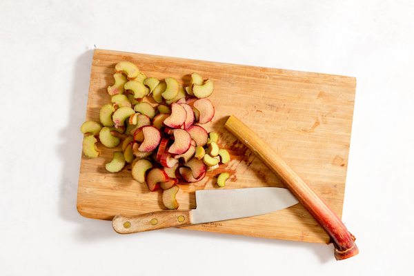 a cutting board, kitchen knife, and rhubarb, partially sliced.
