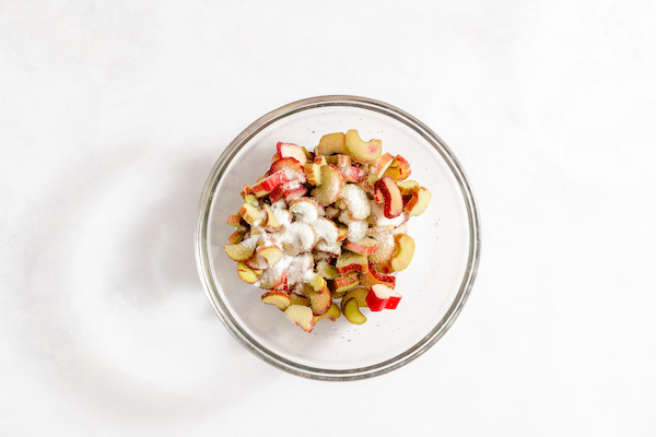 A bowl of sliced rhubar, with sugar and lemon juice, ready to be combined. 