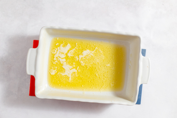 Image, taken from above, shows a white baking dish with melted butter in the bottom. 