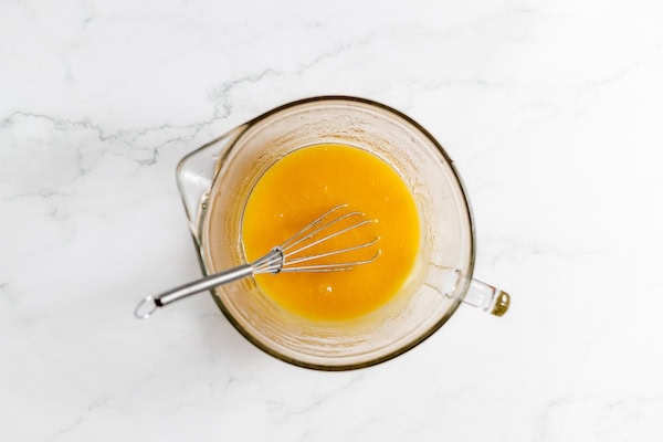 Image shows a glass mixing bowl with the wet ingredients all combined and a whisk resting in it