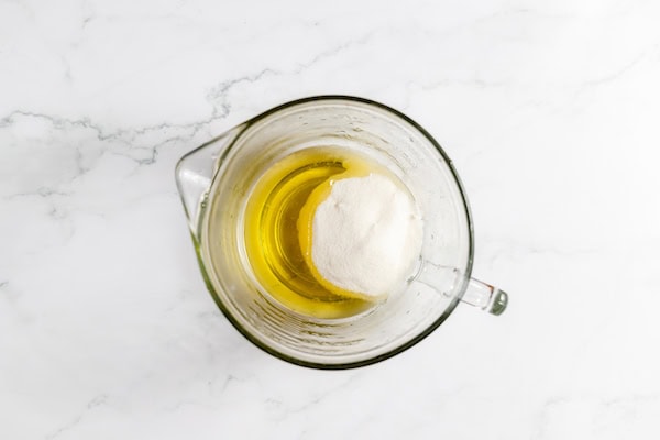 Image shows a glass mixing cup with oil and sugar together