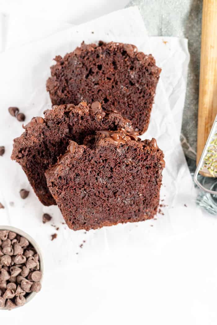 Photo, taken from above, shows three slices of chocolate zucchini bread on a napkin. Nearby is a small bowl of chocolate chips