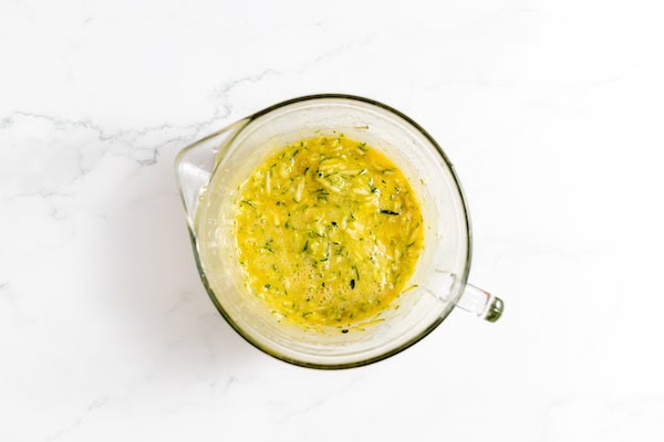 Image shows a glass mixing cup with zucchini bread batter ready to mix in the dry ingredients