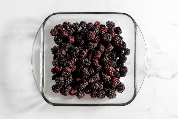 Image, taken from above, shows a square pan full of blackberries. 