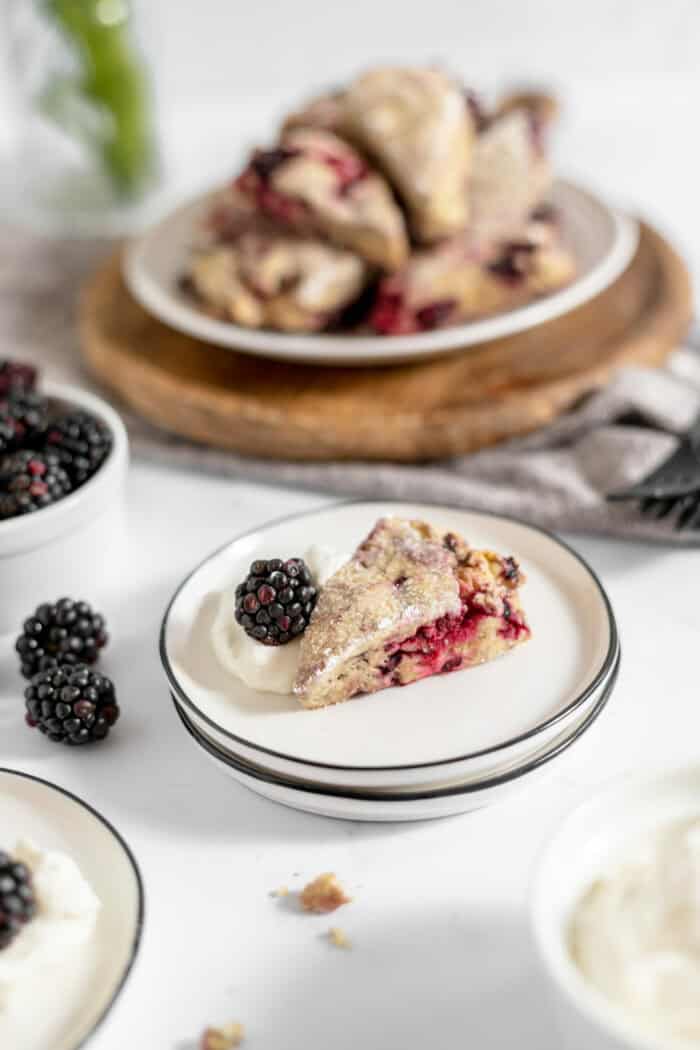 Image shows blackberry scones on a plate with whipped cream